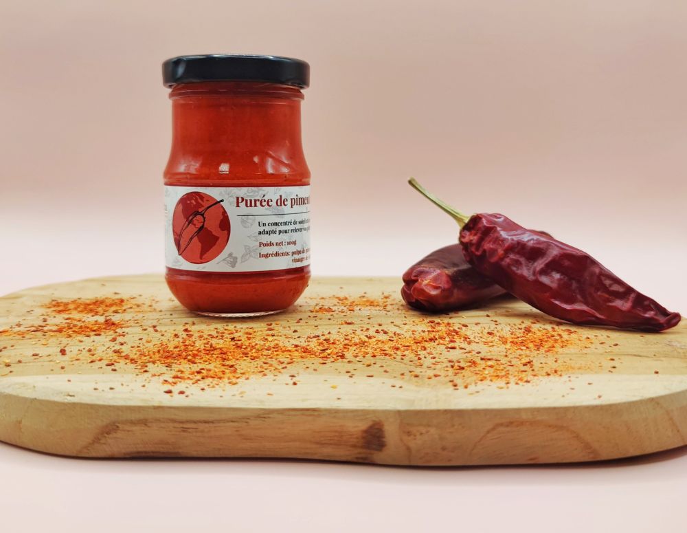 Purée de piment d'Espelette AOP Origine France 100g, présentation dans un pot sur planche en bois avec piments d'Espelette entiers